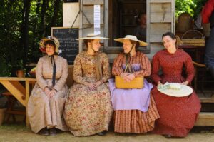 A group of women dressed in Victorian era clothing sit on a wooden bench at Columbia State Historic Park.