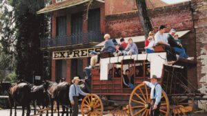 A group of people sitting on a horse drawn wagon in front of a building in Columbia State Historic Park.